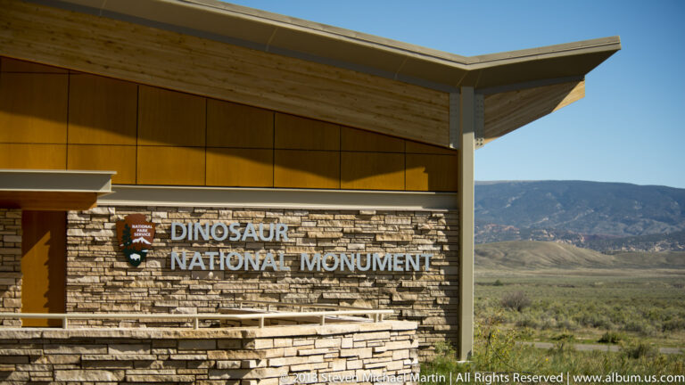 Visitor center with “Dinosaur National Monument” lettering on a stone wall and mountains beyond.