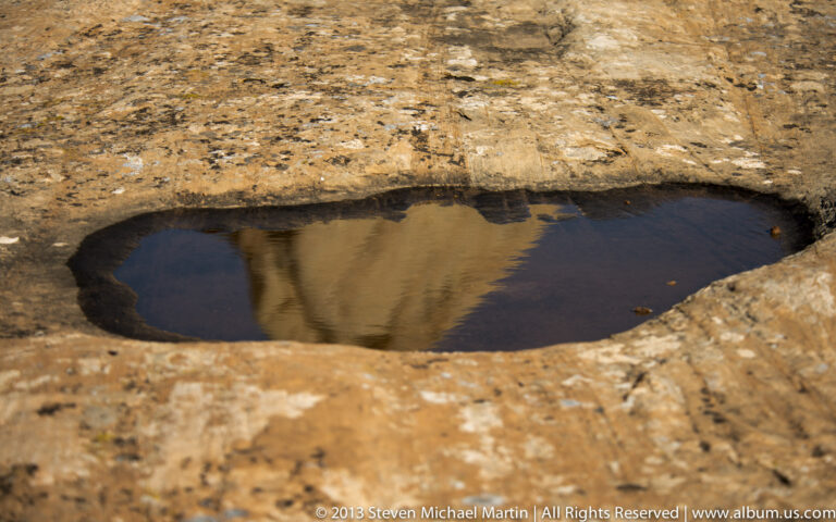 Dark pool reflects a sandstone wall inside a smooth oval depression in the rock.