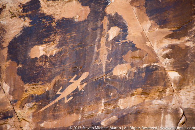 Pale linear figures and marks appear on a dark red sandstone panel.