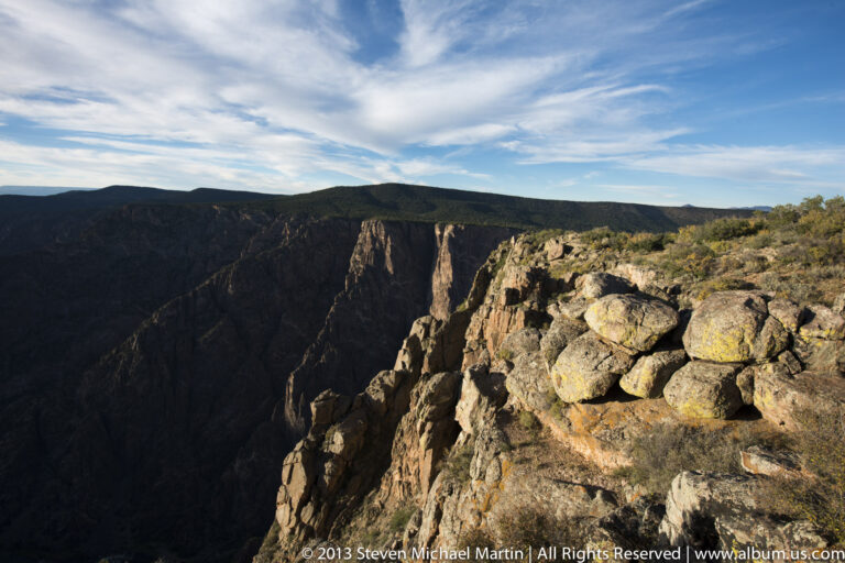 Pale boulders line the canyon rim above shadowed vertical walls and sunlit cliffs across the gorge.