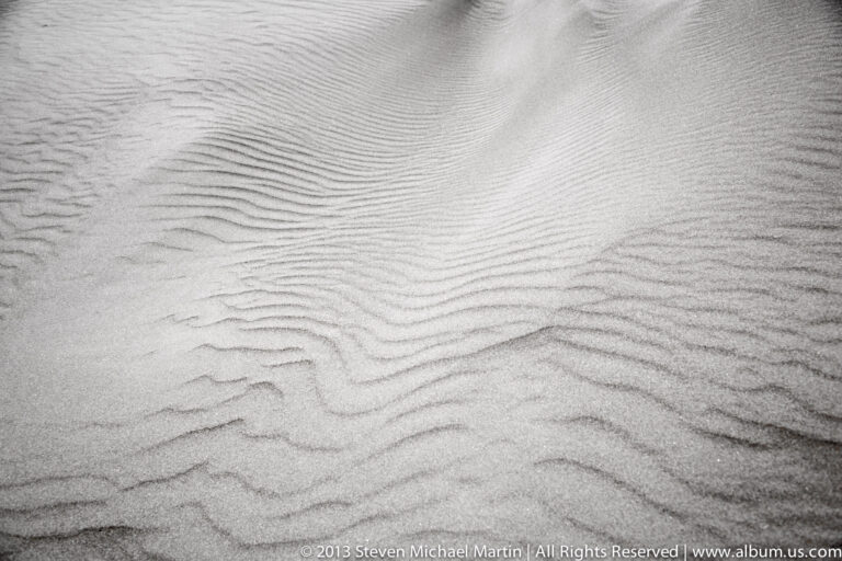 Closely spaced curved ripples cover pale sand, forming a shallow trough near the upper edge.