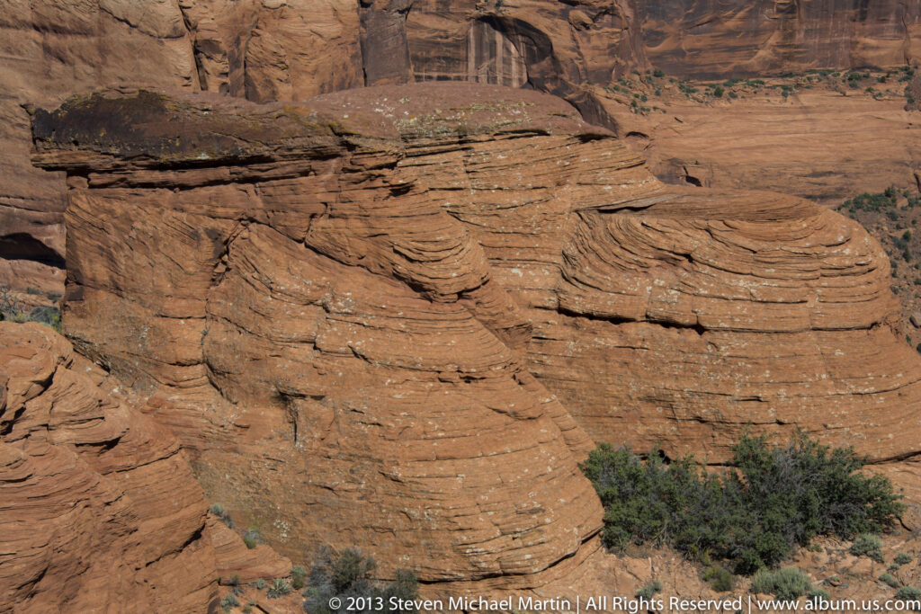 A projecting red sandstone shelf shadows thin horizontal rock layers above scattered shrubs.