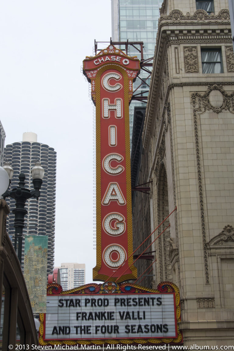The red Chicago Theatre sign and concert marquee rise beside an ornate stone facade and modern city towers.