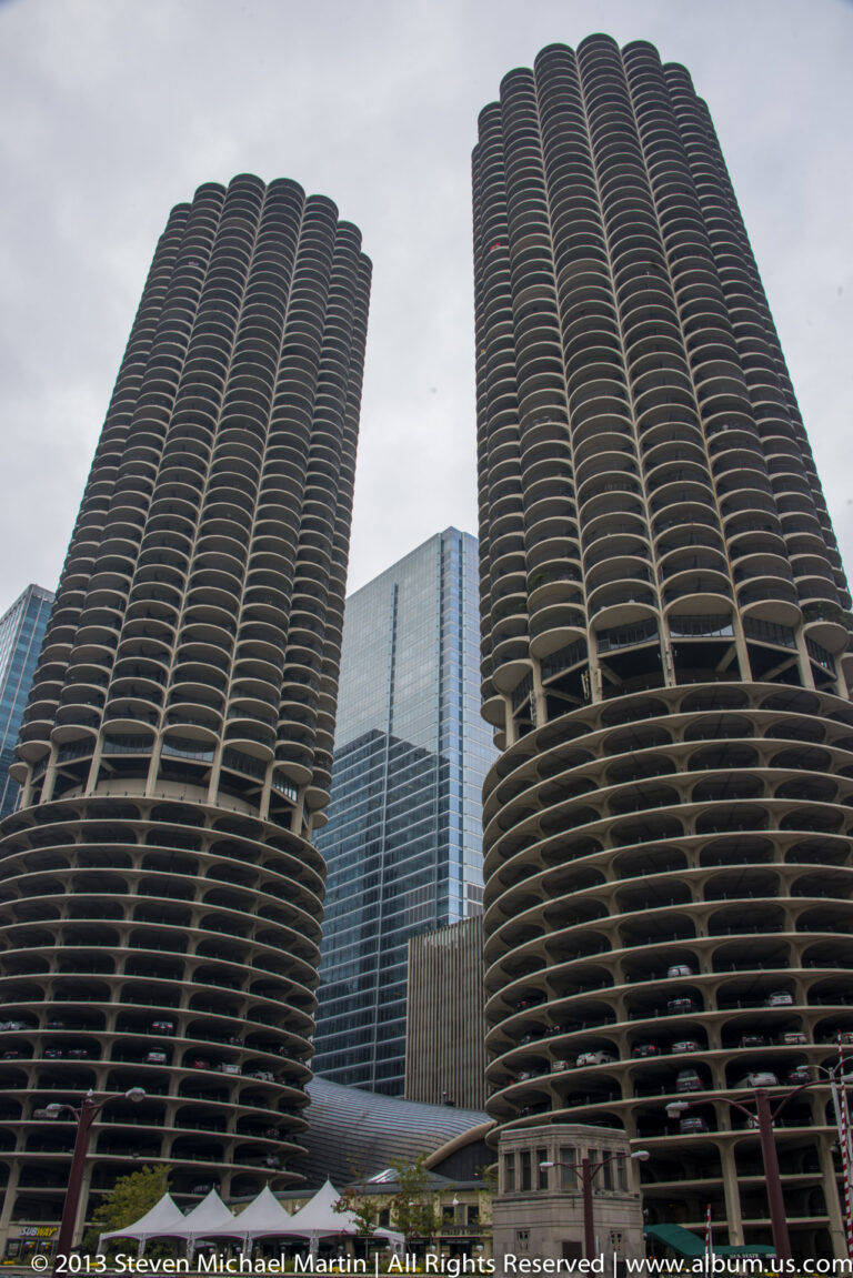 Two cylindrical towers with repeating curved balconies rise above neighboring glass buildings.