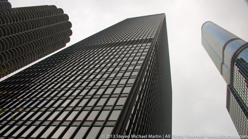 Dark gridded, curved glass, and rounded balcony facades converge overhead around a pale sky.