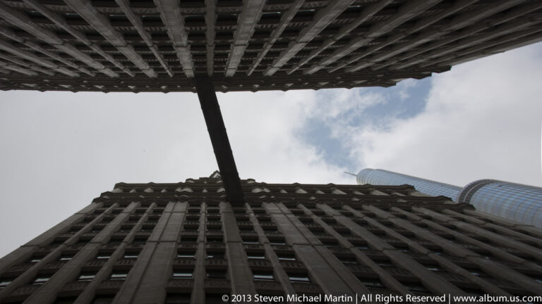 High-rise walls and an overhead structure frame a narrow patch of sky, crossed by a diagonal support.