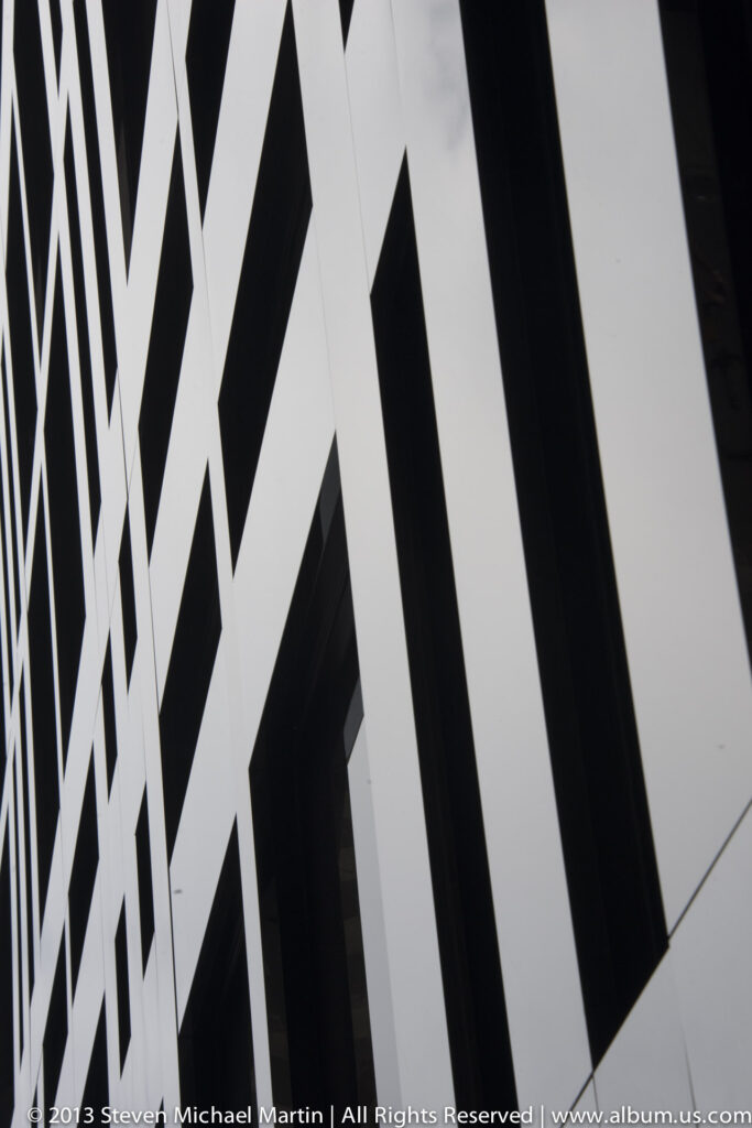 Black diagonal bands divide white wall panels and dark windows in a close view of a modern facade.