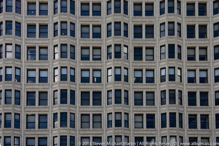 Rows of recessed rectangular windows repeat between projecting stone piers across a pale office facade.