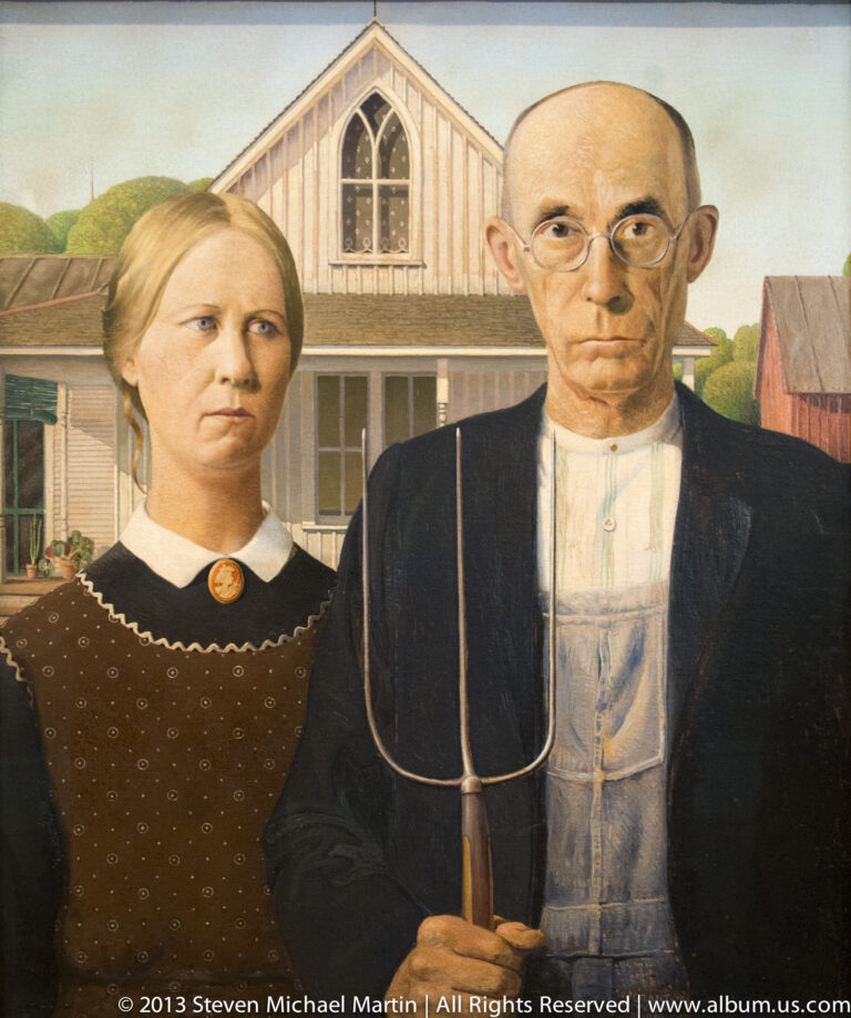 A stern woman and man stand before a farmhouse, the man holding a pitchfork in Grant Wood’s American Gothic.