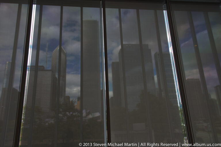 Dark glass panes reflect neighboring skyscrapers and clouds, divided by narrow vertical mullions.
