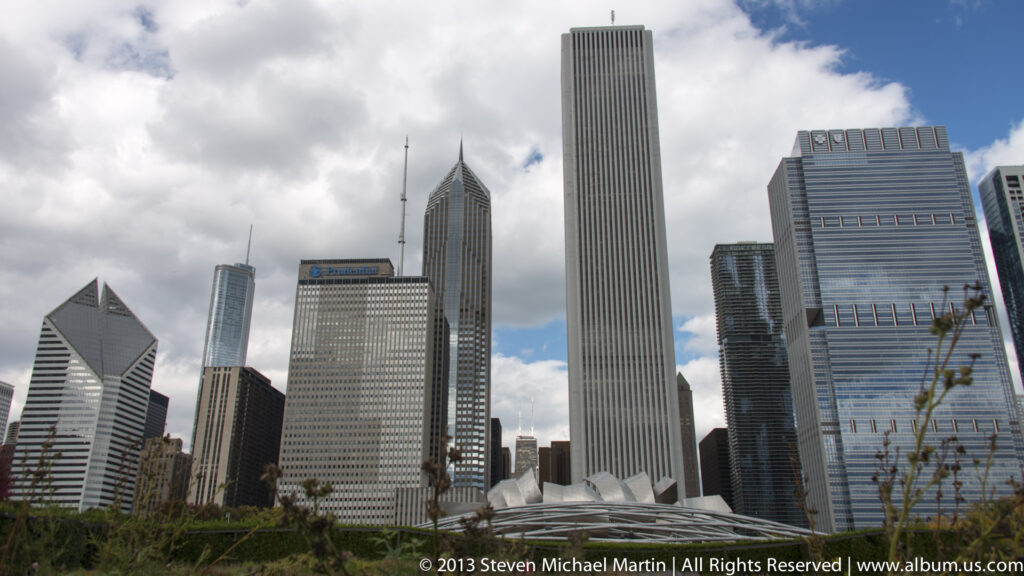 Several downtown towers rise beneath broken clouds, including a ribbed rectangular skyscraper and a pointed-roof high-rise.