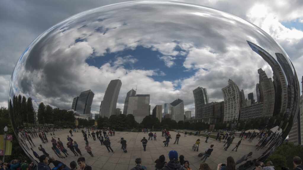 Cloud Gate reflects a curved skyline, blue sky, clouds, and plaza visitors across its polished steel surface.