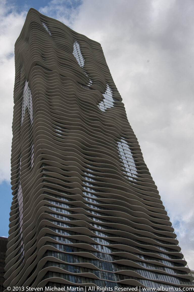 Rounded balcony bands ripple across a high-rise facade, with irregular openings revealing blue glass and sky.