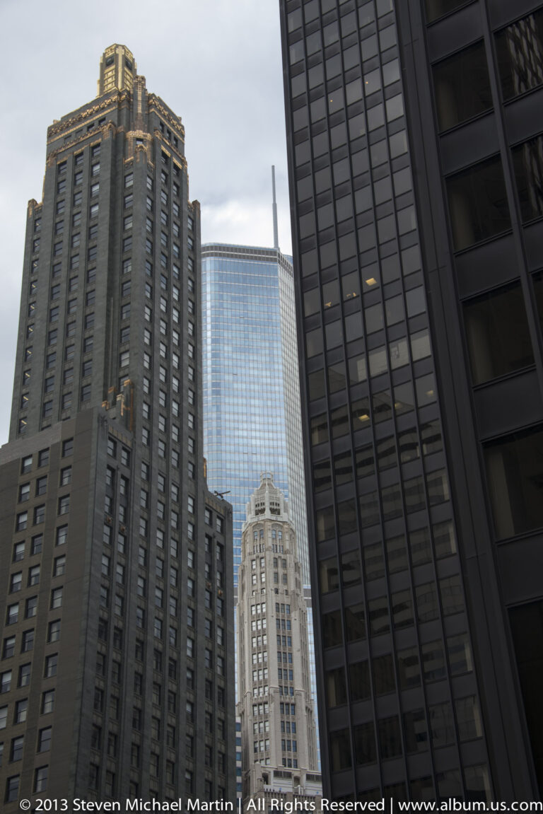 A blue glass tower and pale crowned building appear between dark and brown office facades.