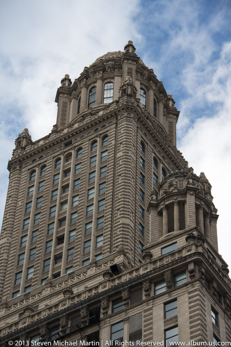 A pale stone high-rise with carved bands, arched upper windows, and an ornate crown rises against clouds.