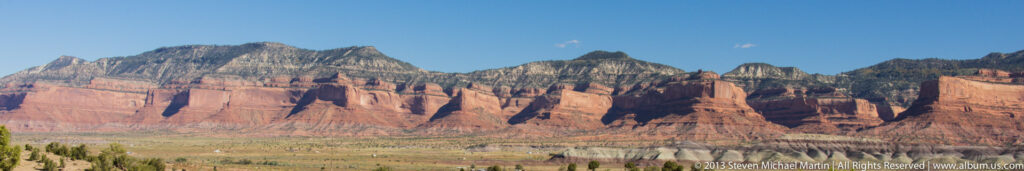 A jagged mountain skyline rises above rust-red lower slopes and a narrow foreground band of trees.