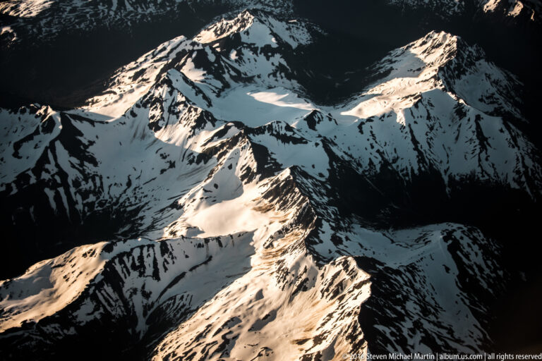 Sunlit glacier ice runs between steep, shadowed mountain ridges, with snow along the central slopes.