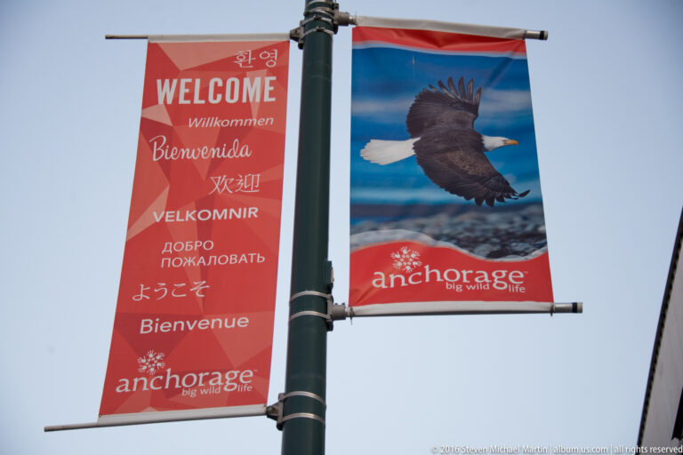 Two Anchorage street banners show multilingual welcome messages and a bald eagle image.