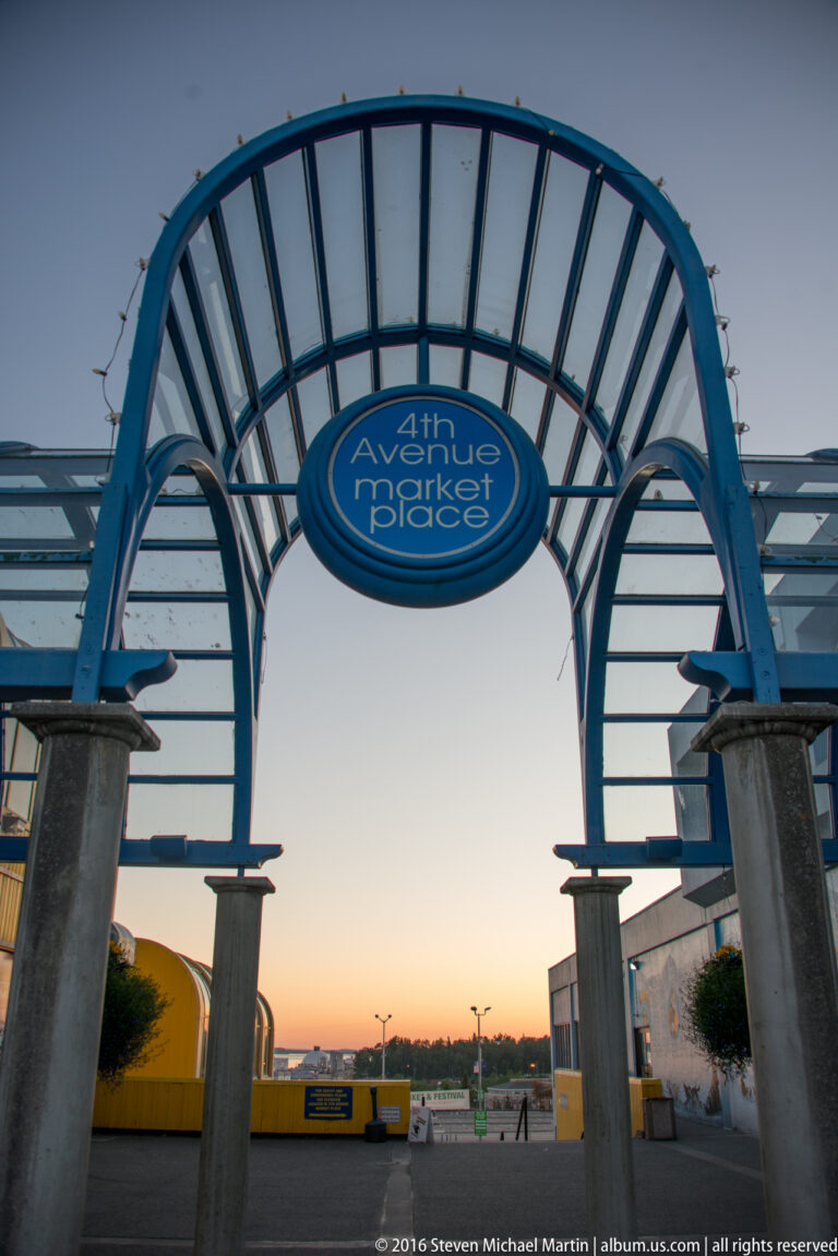 A blue arched gateway marked 4th Avenue Market Place frames a plaza at dusk.