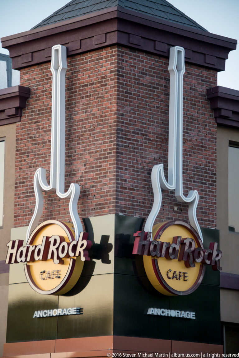 Two guitar-shaped Hard Rock Cafe signs marked Anchorage project from a brick facade.