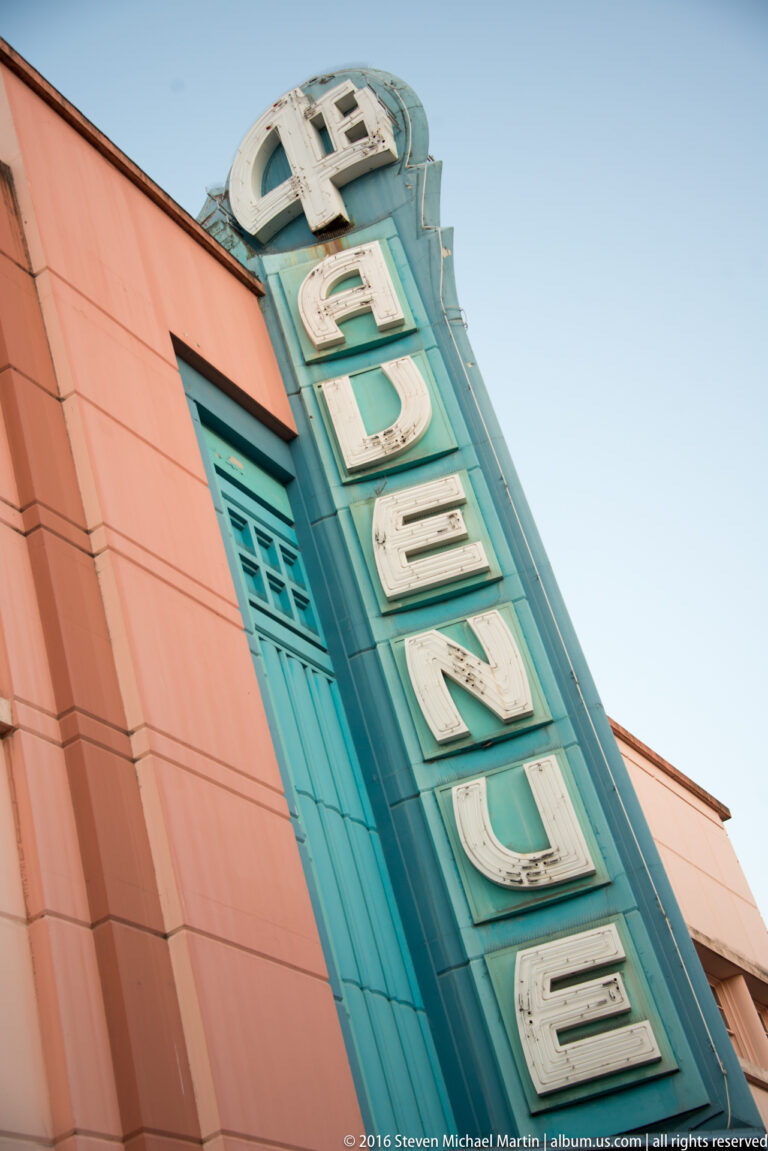 Cream letters spelling Hotel Captain Cook project from a blue-green panel on a salmon-colored facade.