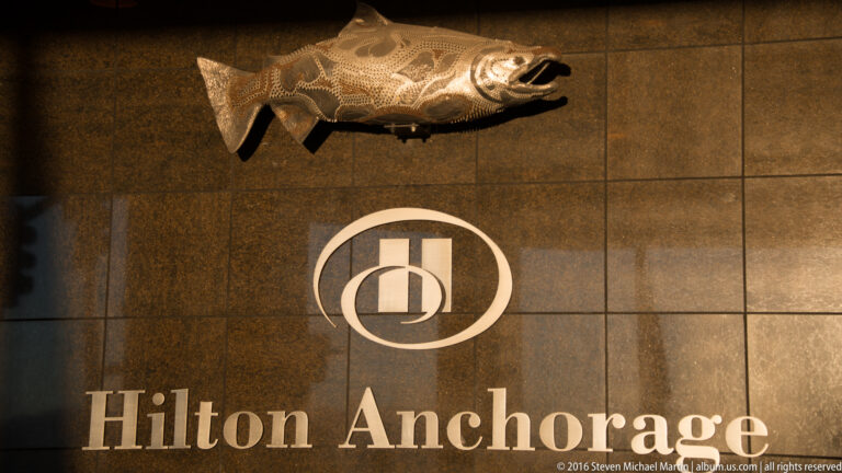 Hilton Anchorage lettering and circular emblem illuminated on a dark stone-tiled wall.