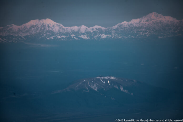 Distant snow-covered summit tinted pink above dark ridges and blue evening haze.