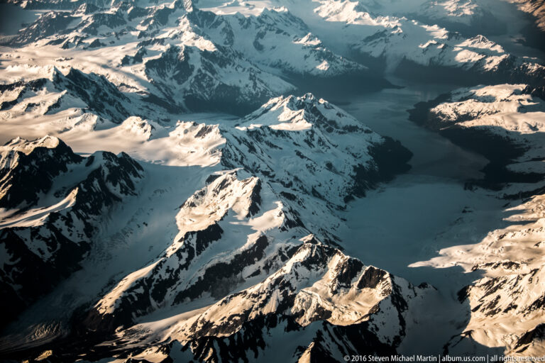 A glacier winds through a steep valley enclosed by jagged snow-covered peaks.