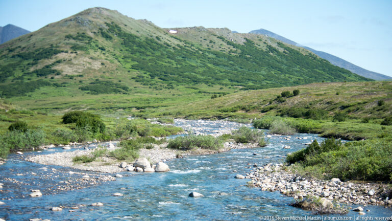 A rocky stream winds through a green tundra valley beneath rounded hills.