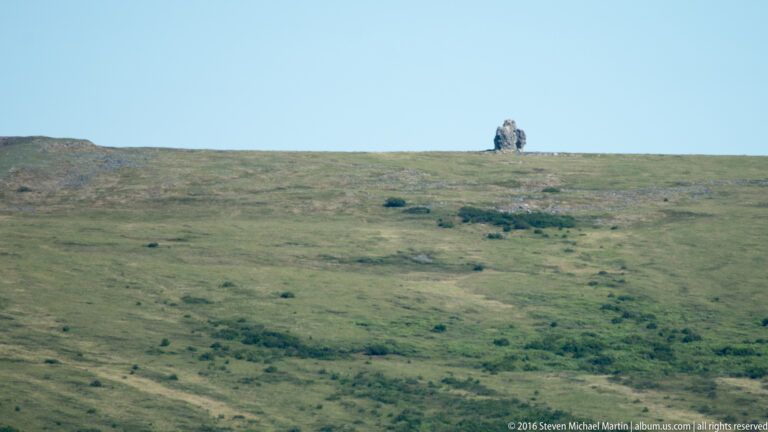 A small jagged rock outcrop stands alone on a broad tundra ridge.