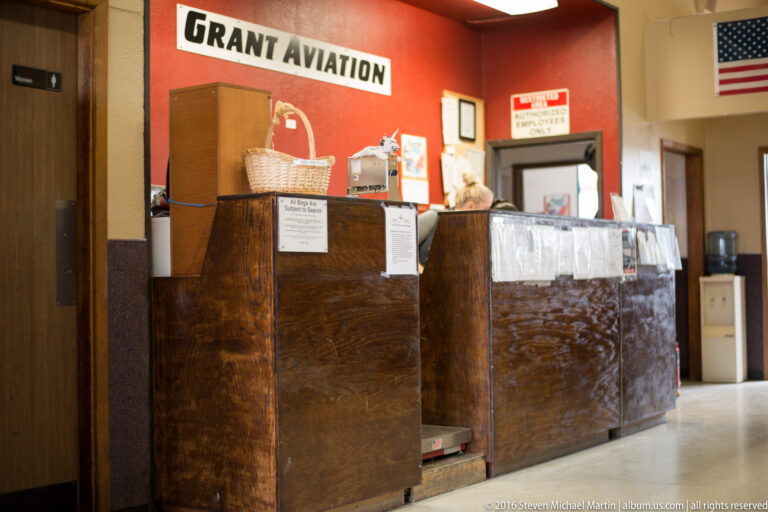Wooden service counters beneath a red Grant Aviation wall, with posted notices, an open doorway, and a U.S. flag.