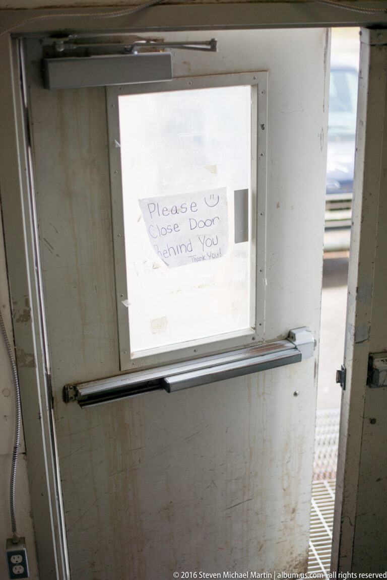 Handwritten request to close the door taped to a small window above a horizontal metal push bar.