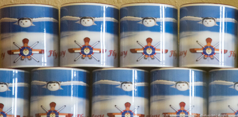 Rows of blue-and-white mugs bearing a repeated airplane emblem and partial red lettering.