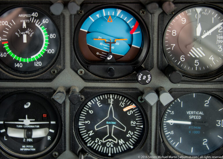 Cockpit close-up of a blue-and-brown attitude indicator surrounded by speed, clock, navigation, and vertical-speed gauges.