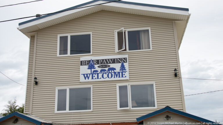 Tan multi-story building with a blue “Bear Paw Inn Welcome” sign featuring bears and evergreen trees.