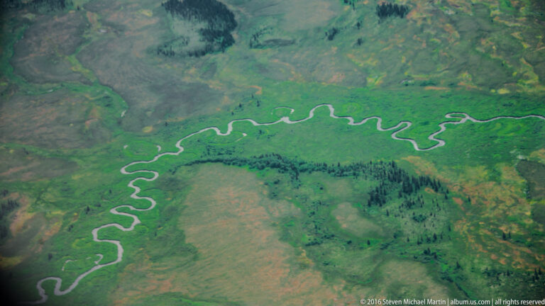 A pale, tightly winding channel cuts through bright green marshland and low vegetated islands.