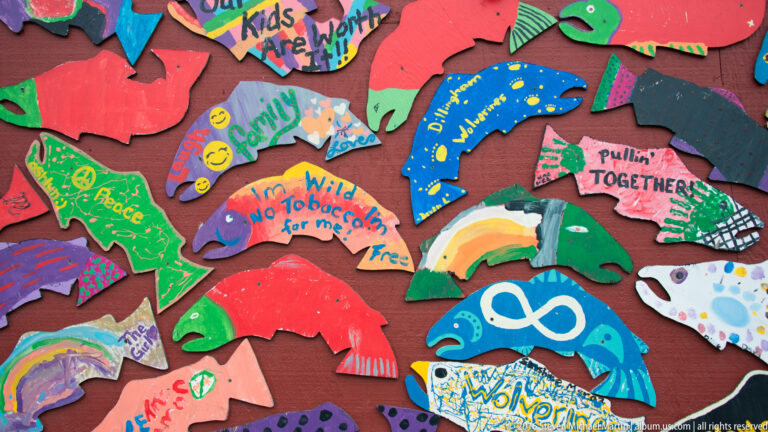 Close view of colorful fish-shaped panels with handwritten messages, patterns, and an infinity symbol on a red wall.