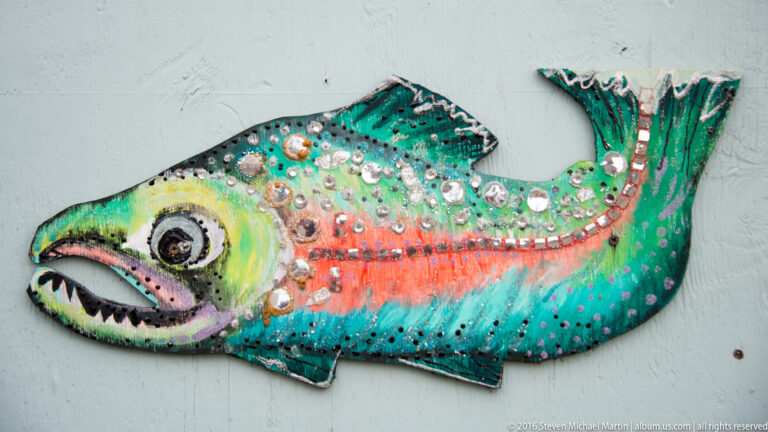 Colorful fish-shaped wall sculpture with raised circular decorations, a large eye, and an open toothed mouth.