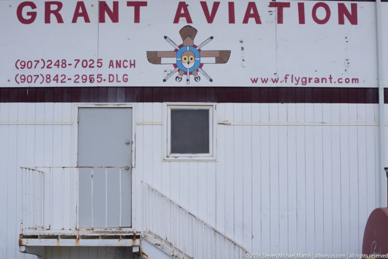 Close view of a Grant Aviation wall sign with an aircraft emblem above a weathered door and metal landing.