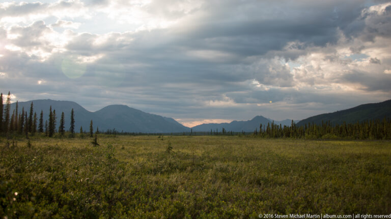 Evening clouds cast shadows across an open plain and mountain valley.