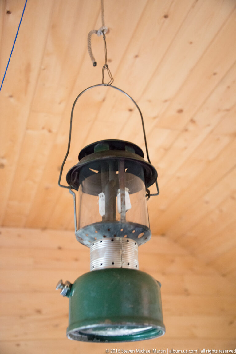 Green metal lantern with a glass globe hangs from a wooden cabin ceiling.