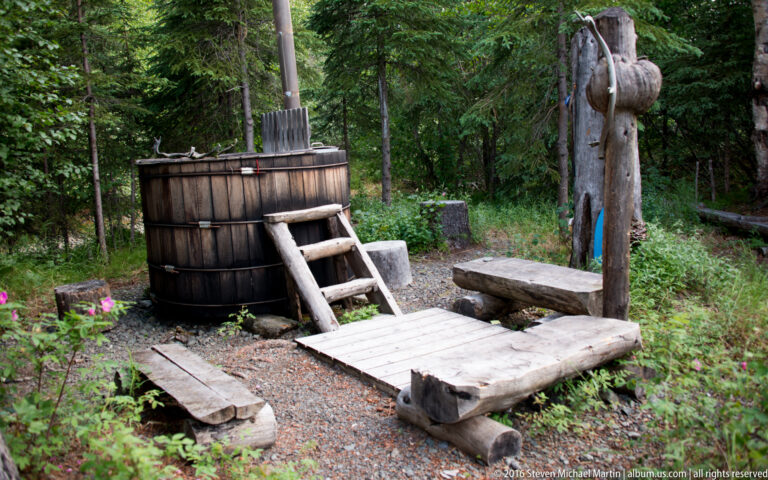 Round wooden tub with steps and a low platform in a forest clearing.