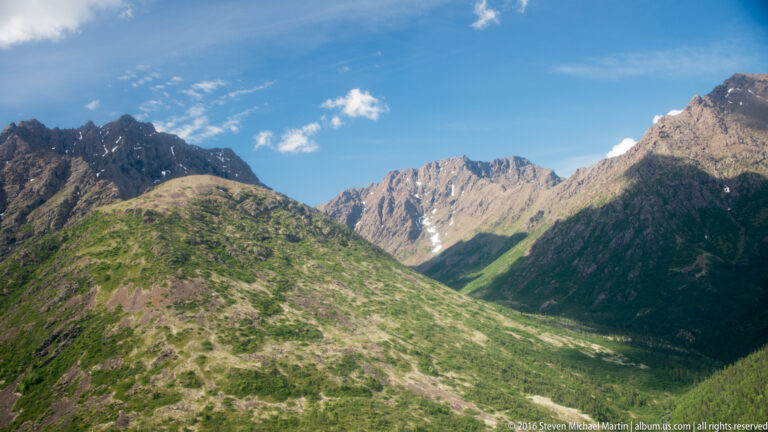 Green ridges frame a mountain pass leading toward a jagged central peak with a small snow patch.