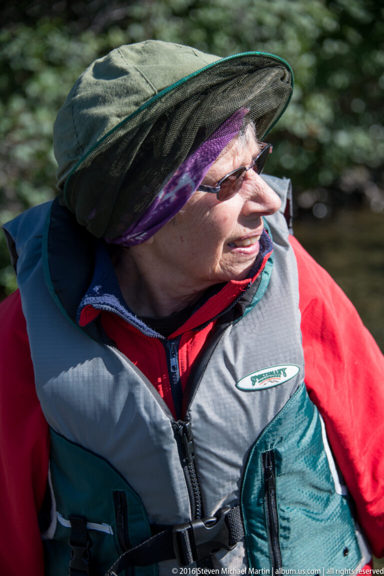 Close profile of a woman in glasses, a wide-brim hat, and a gray life vest.