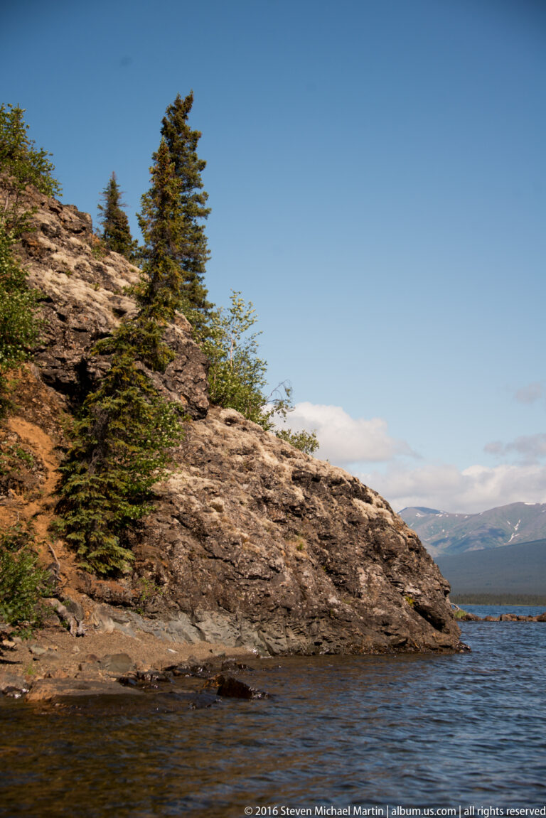 Rocky outcrop with spruce trees projects into the lake beneath a clear sky.