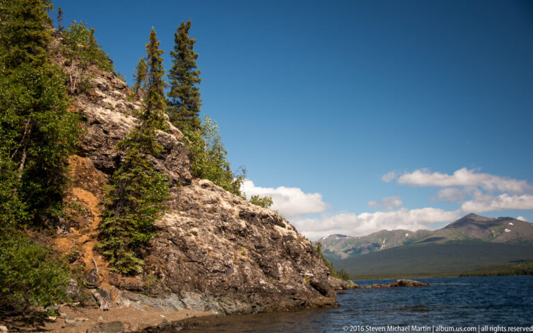 Rocky, tree-covered point frames rippled lake water and distant hills.