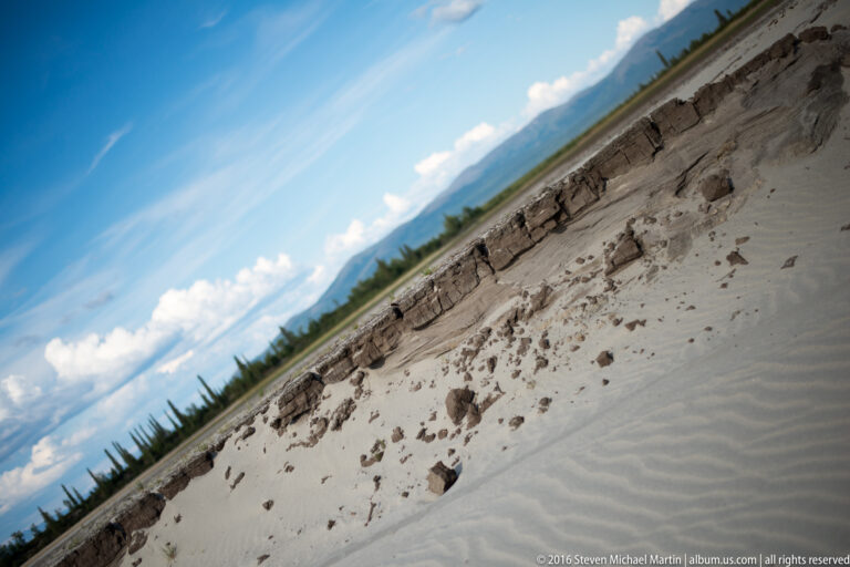 A tilted view shows a pale eroding bluff with broken sediment blocks above a sandy shore.