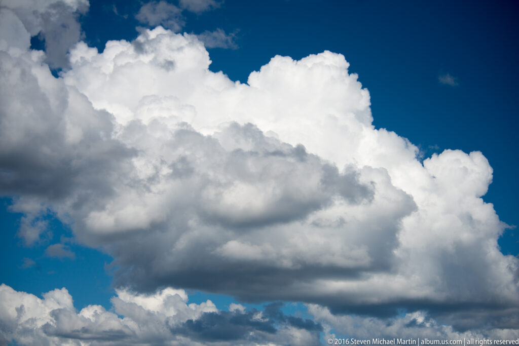 A towering white cumulus cloud with gray undersides rises against a deep blue sky.