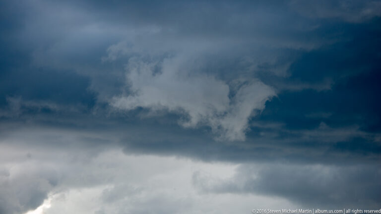 Layered blue-gray storm clouds fill the frame, with a pale opening near the center.