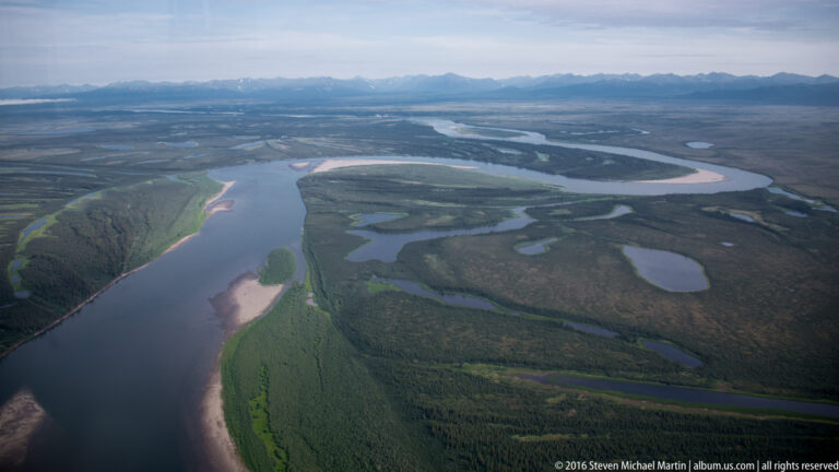 A wide river bends through low tundra past smaller lakes and ponds beneath distant mountains.